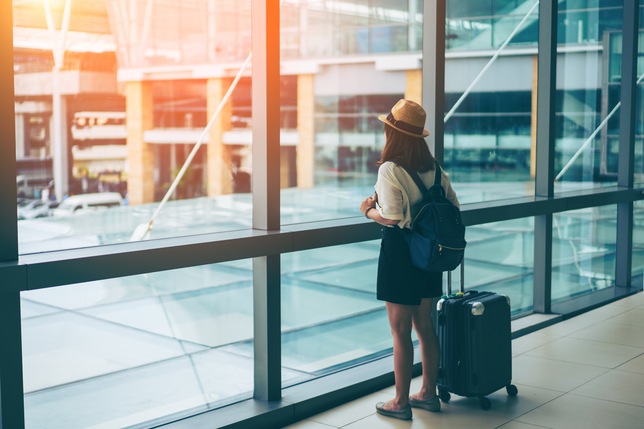 young asian woman with baggage looking through the window of an airport departure
